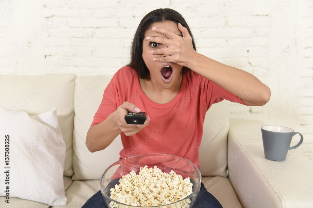 Naklejka premium latin woman sitting at home sofa couch in living room watching television scary horror movie