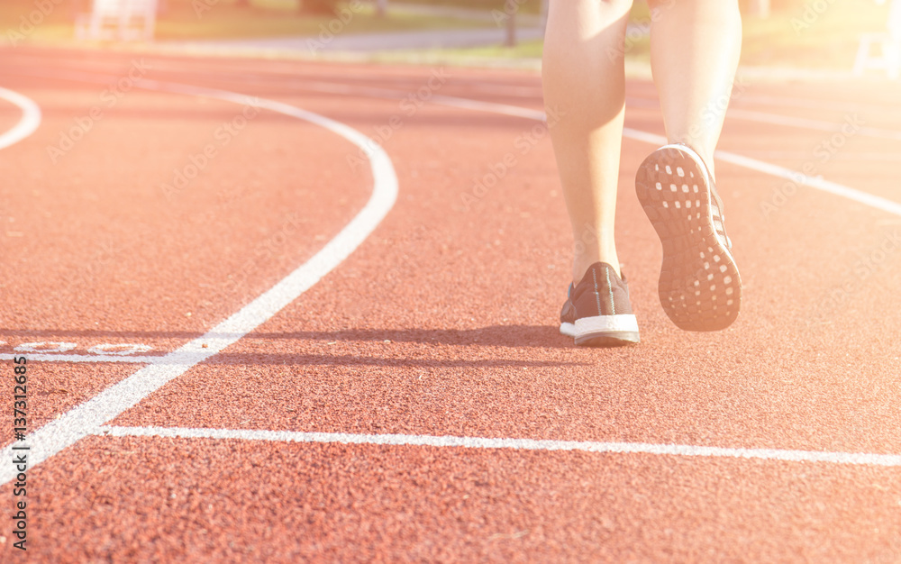 Running sport. Woman runner legs and shoes in action on track outdoors at sunset.