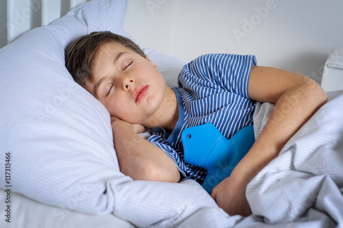 Canvas Print Kind liegt mit Wärmflasche und Bauchweh krank im Bett