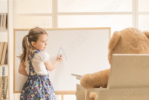 Cute toddler playing teacher role game with her toy. Little girl teaching her Teddy bear friend alphabet. Learning letters. Learn Study Education School Knowledge Concept