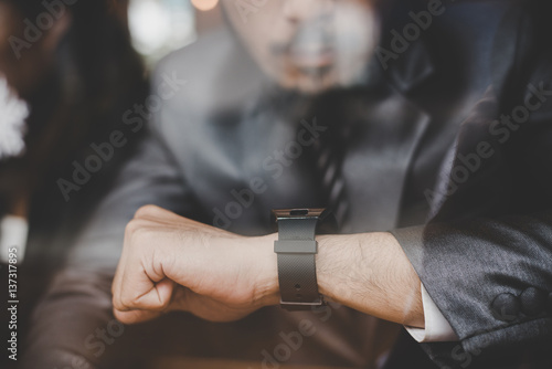 Young businessman sitting at cafe bar,looking at watch.