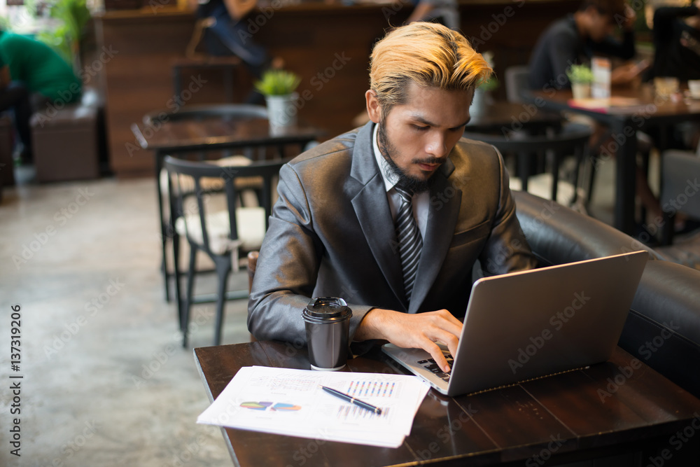Young businessman holding cup of coffee while working on laptop computer in coffee shop.