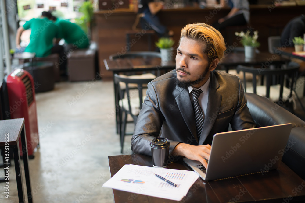 Young businessman holding cup of coffee while working on laptop computer in coffee shop.