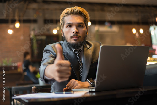 Businessman thumbs up while working with laptop computer at coffee shop.