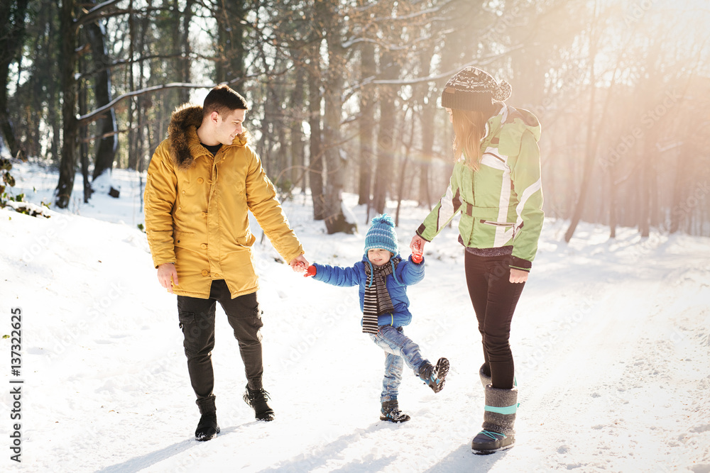Little boy enjoying playing with his young mom and dad. Toddler kid holding hands with parents. Children play outdoors in snow. Kids sled in winter park. Outdoor active fun for family vacation.