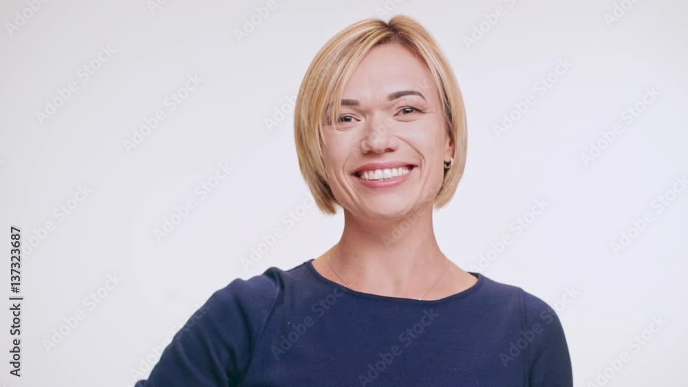 Joyful Caucasian blonde female in blue sweatshirt smiling laughing waving hand on white background in slowmotion Joyful Caucasian blonde female in blue sweatshirt smiling laughing waving hand on white background in slowmotion