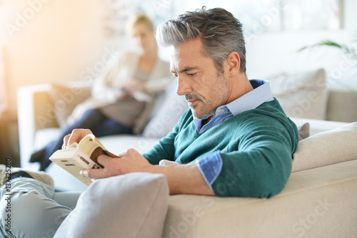 Couple at home reading book, man in foreground photo