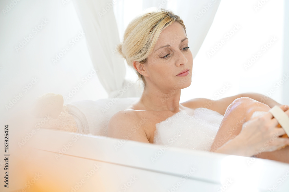 Naklejka premium Blond woman in bathtub massaging her legs