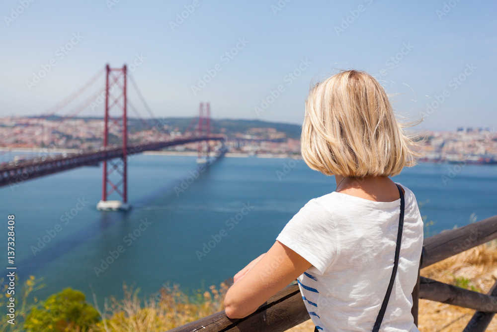 Fototapeta premium Female traveler standing next to the statue of National Sanctuary of Christ the King and enjoys panoramic views of Lisbon and the bridge of April 25.
