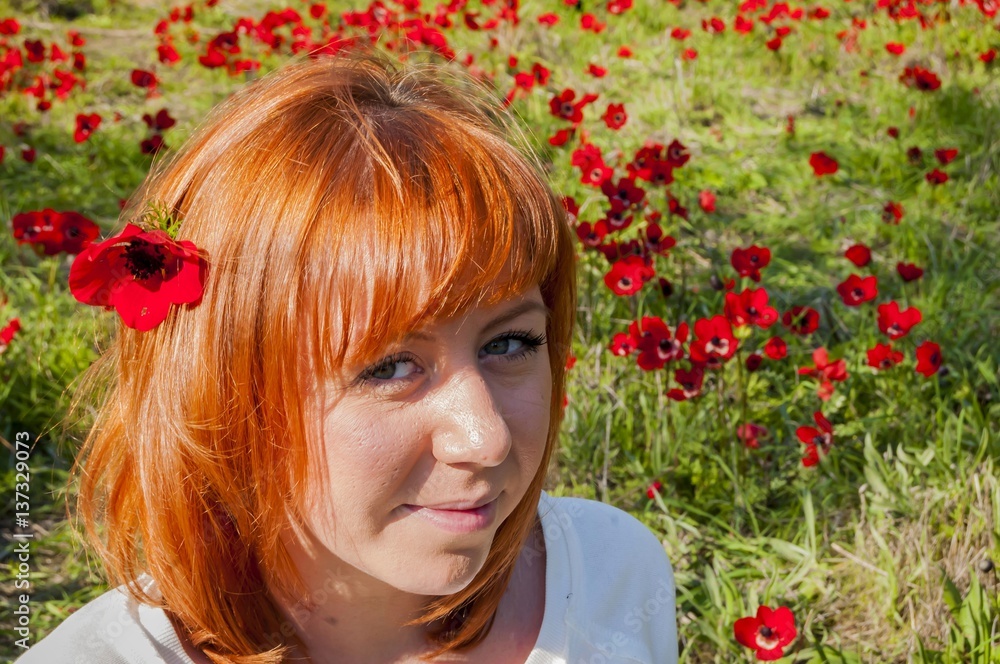 Naklejka premium Pretty girl with a red flower behind her ear at the anemone flowering field. Flowering Negev Desert in Israel.