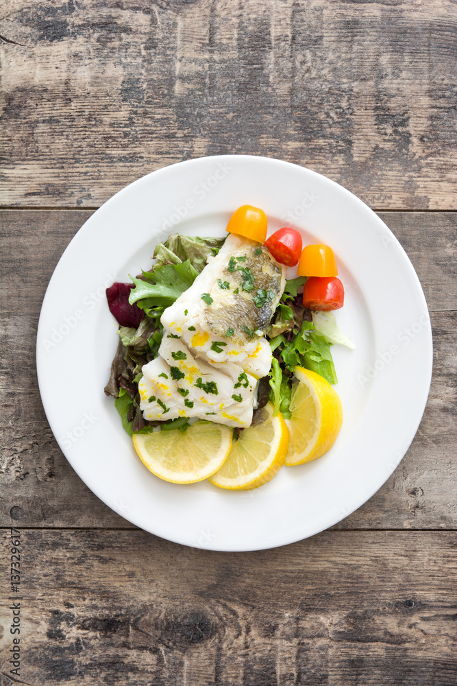 Fried cod fillet and salad in plate on wooden background
