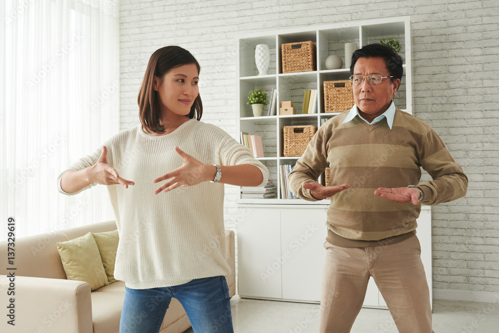 Obraz premium Portrait of pretty young woman and her senior father standing in living room and doing breathing exercises