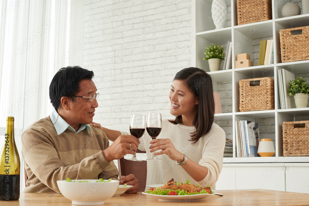 Senior Asian man and his young daughter celebrating Fathers Day together: they holding glasses of wine in hands and clinking them together Senior Asian man and his young daughter celebrating Fathers Day together: they holding glasses of wine in hands and clinking them together