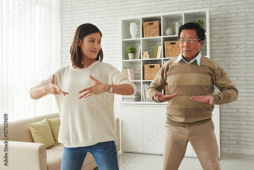 Portrait of pretty young woman and her senior father standing in living room and doing breathing exercises