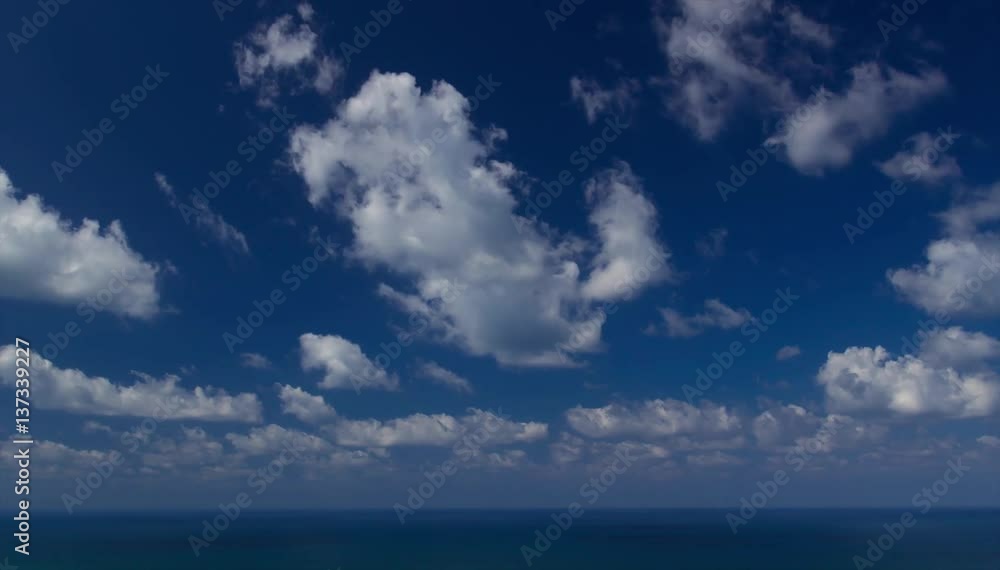 Timelapse of Clouds crossing the blue sky above the sea or ocean. The clouds are white and gray and cross from right to left. The clouds are reflected in the water. Timelapse of Clouds crossing the blue sky above the sea or ocean. The clouds are white and gray and cross from right to left. The clouds are reflected in the water.