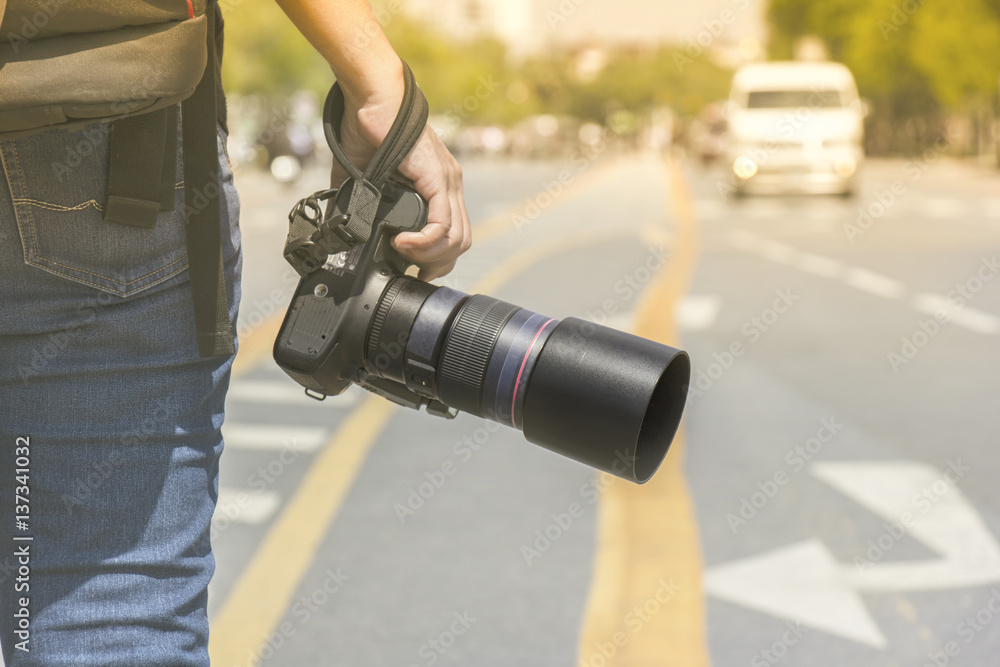 Photographer holding a camera standing on the street in the morning light with blur background and bokeh. Photographer holding a camera standing on the street in the morning light with blur background and bokeh.