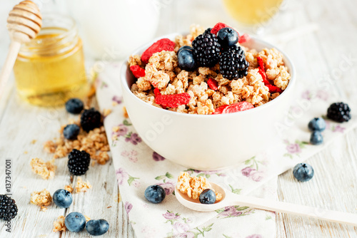  healthy and hearty breakfast of muesli , oatmeal or granola with berries , blackberries , blueberries and strawberries , honey , milk and green tea on a wooden background