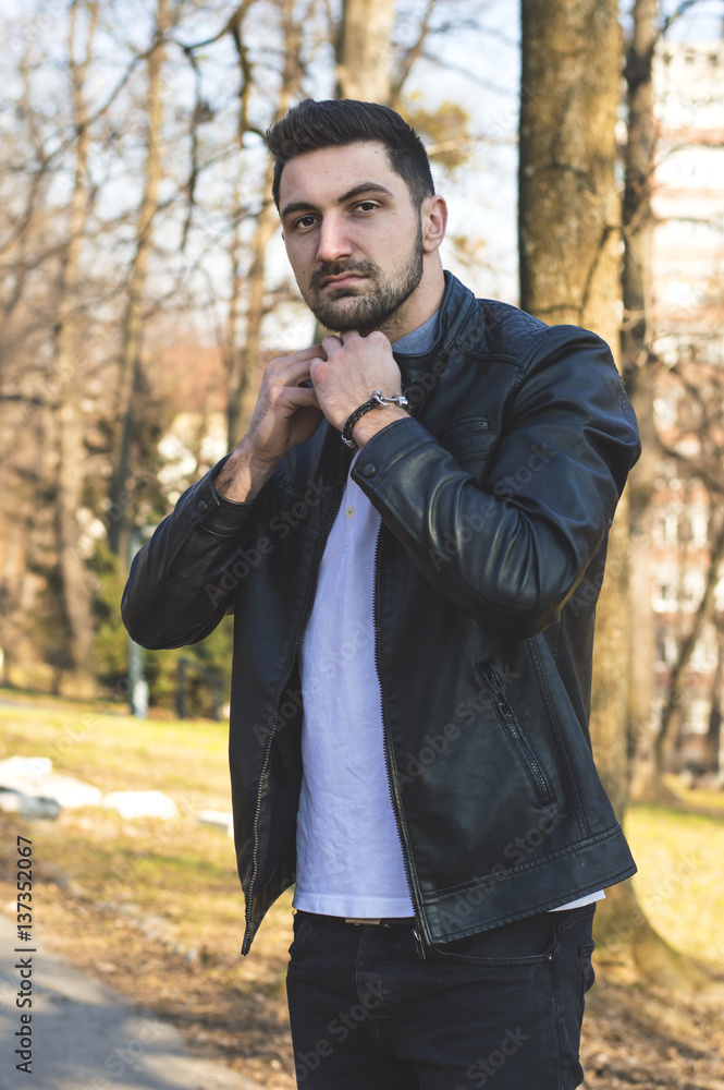 Handsome man posing outdoors wearing fashionable clothes in the urban environment and in the park surrounded by nature and trees on a sunny day. Buttoning up his shirt. Handsome man posing outdoors wearing fashionable clothes in the urban environment and in the park surrounded by nature and trees on a sunny day. Buttoning up his shirt.