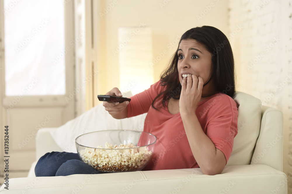Naklejka premium latin woman sitting at home sofa couch in living room watching television scary horror movie