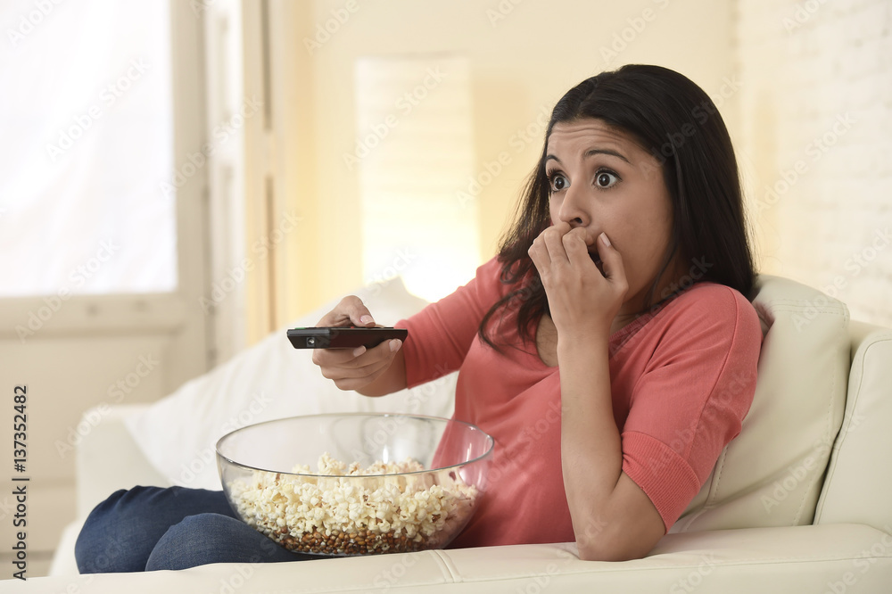 Naklejka premium latin woman sitting at home sofa couch in living room watching television scary horror movie
