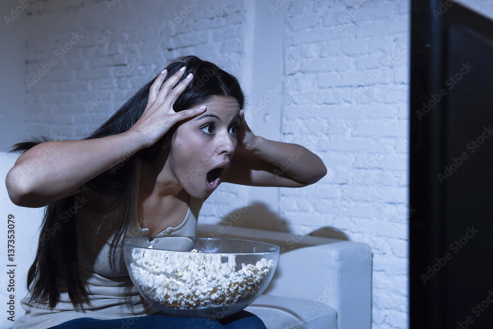 Naklejka premium latin woman at home sofa couch in living room watching television scary horror movie or suspense thriller