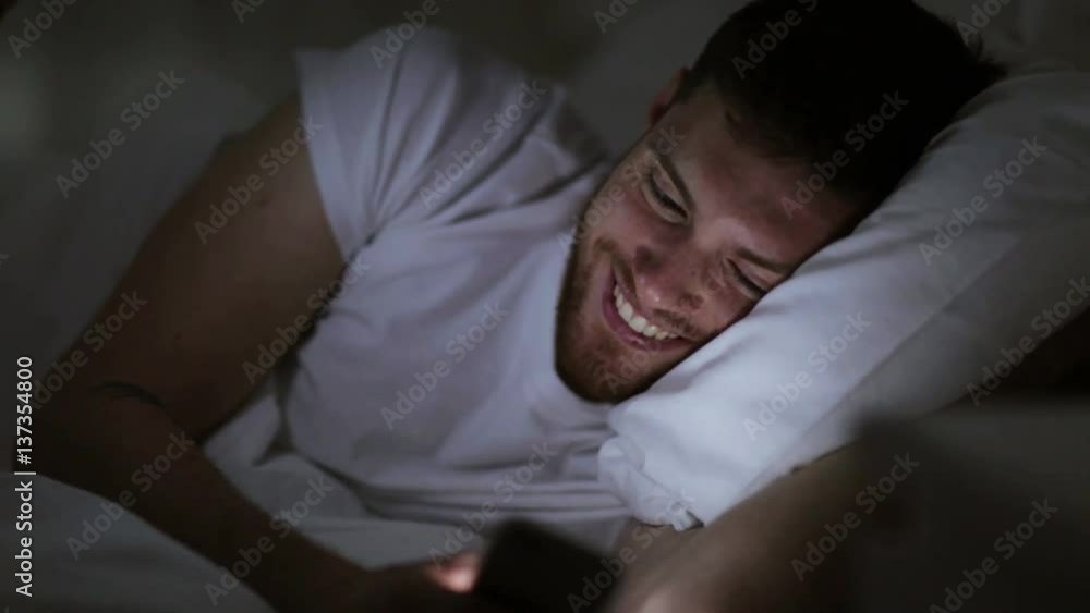 young man with smartphone in bed at night young man with smartphone in bed at night