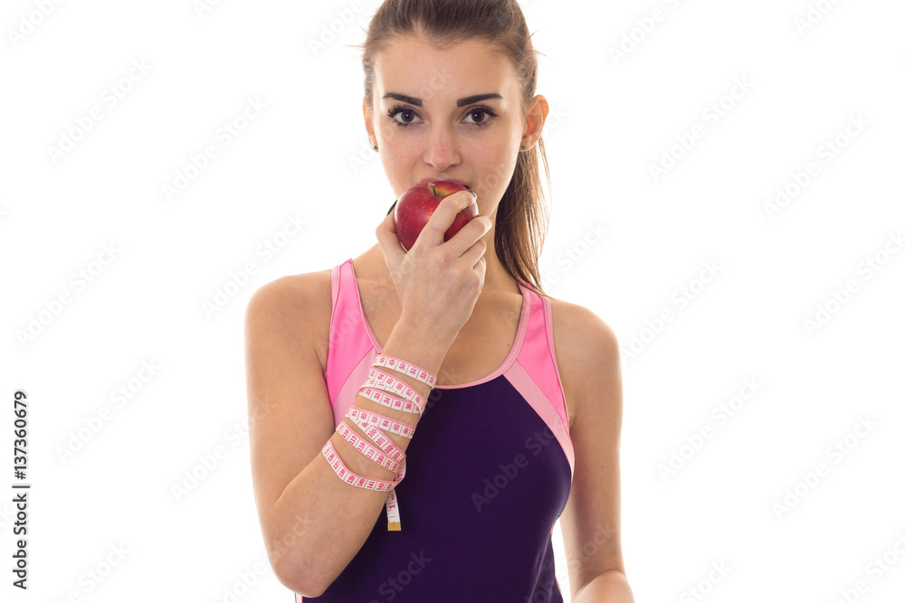 portrait of young slim girl with measure tape on her hand eats red apple and looks at the camera isolated on white background portrait of young slim girl with measure tape on her hand eats red apple and looks at the camera isolated on white background