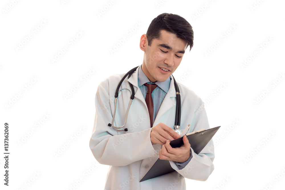 cheerful young brunette man doctor in white uniform with stethoscope make notes isolated in studio cheerful young brunette man doctor in white uniform with stethoscope make notes isolated in studio