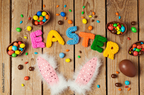 Easter holiday concept with chocolate eggs and bunny ears on wooden background. Top view from above