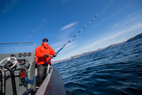 Man with spinning on the boat looking into the distance. Red Jacket. fisherman