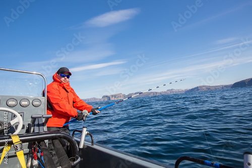 man in a boat with a fishing rod. Red jacket