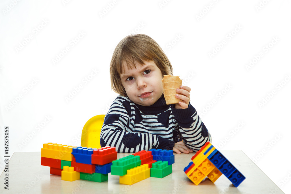 Serious little girl playing in the constructor and eating ice cream. Shooting on a white background. Serious little girl playing in the constructor and eating ice cream. Shooting on a white background.
