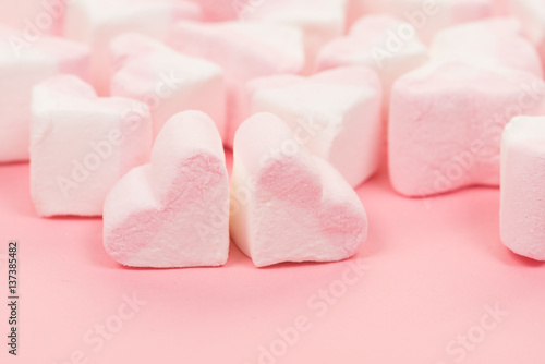 Group of heart shaped pink and white marshmallow candy on a pink background seen from the side