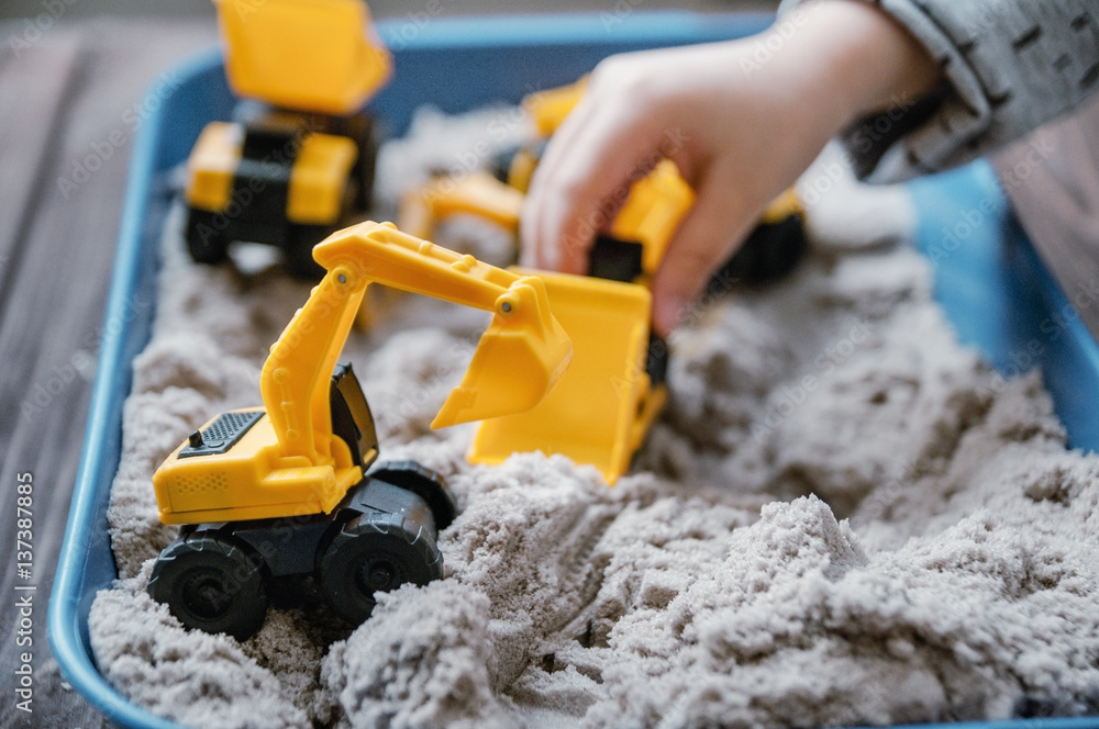 Child playing with kinetic sand and toy construction machinery Child playing with kinetic sand and toy construction machinery