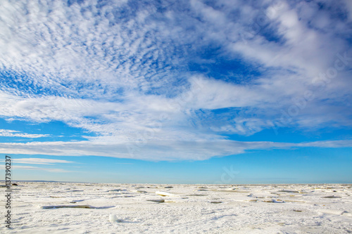 The idyllic panorama of the North sea frozen in the ice. Beautiful nature water frozen in the winter. Landscape snowy expanse to the horizon with a wonderful sky and clouds.