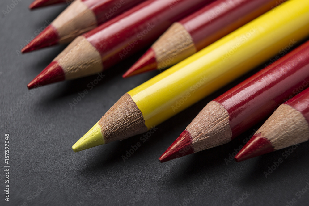 Standing out from the crowd yellow color pencil among red pencils