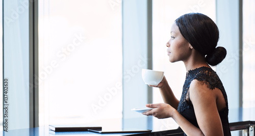 Highly successful young African American woman looking out the window while drinking her morning coffee, while reflecting on her past and thinking about her future.