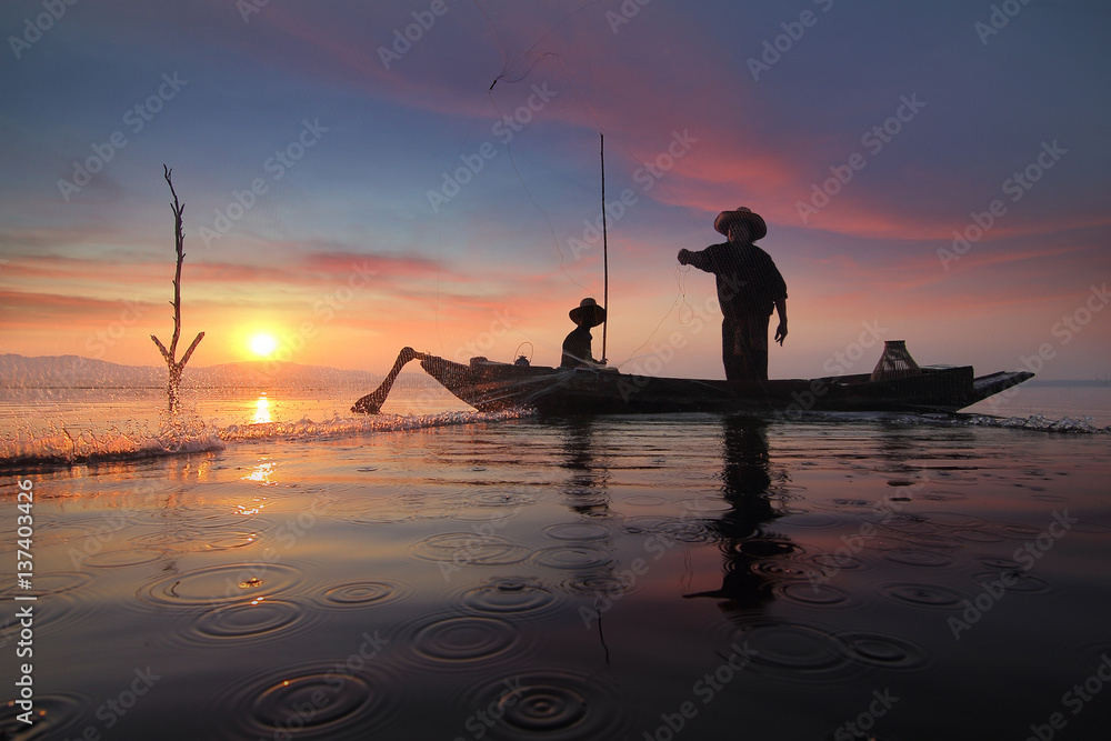 Silhouette of fishermen using nets to catch fish at the Bangpra lake with beautiful scenery of nature during sunrise time. Bang Pra Reservoir at Chonburi province in Thailand