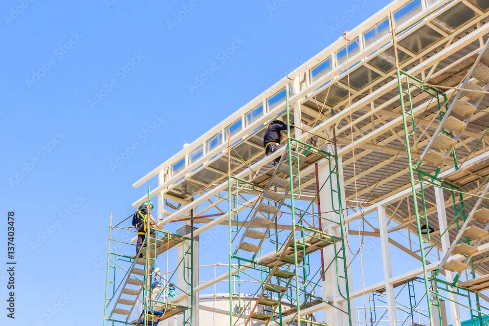 Construction workers working on scaffolding, Man Working on the Working at height with blue sky at construction site Construction workers working on scaffolding, Man Working on the Working at height with blue sky at construction site