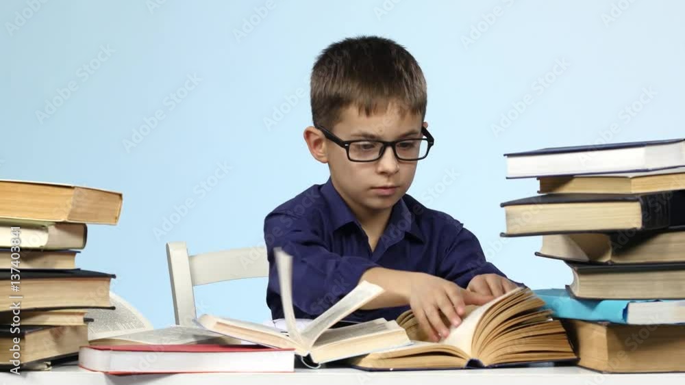 Boy sits at the table and excitedly leafing through the pages of books. Blue background.