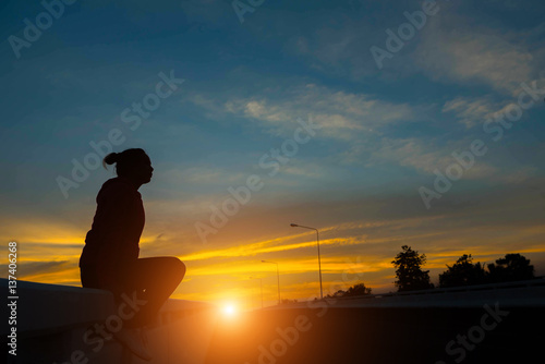 silhouette woman on road watching yellow and orange setting sun at sunset