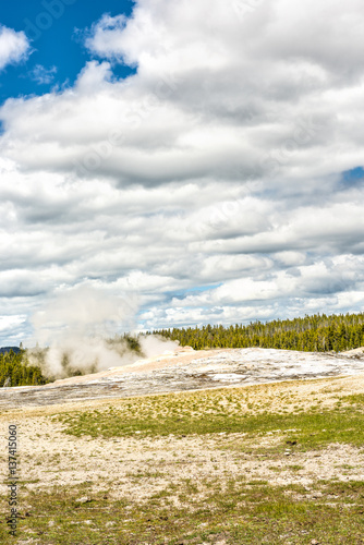 Old Faithful Geyser waiting to erupt in Yellowstone National Park with steam and clouds