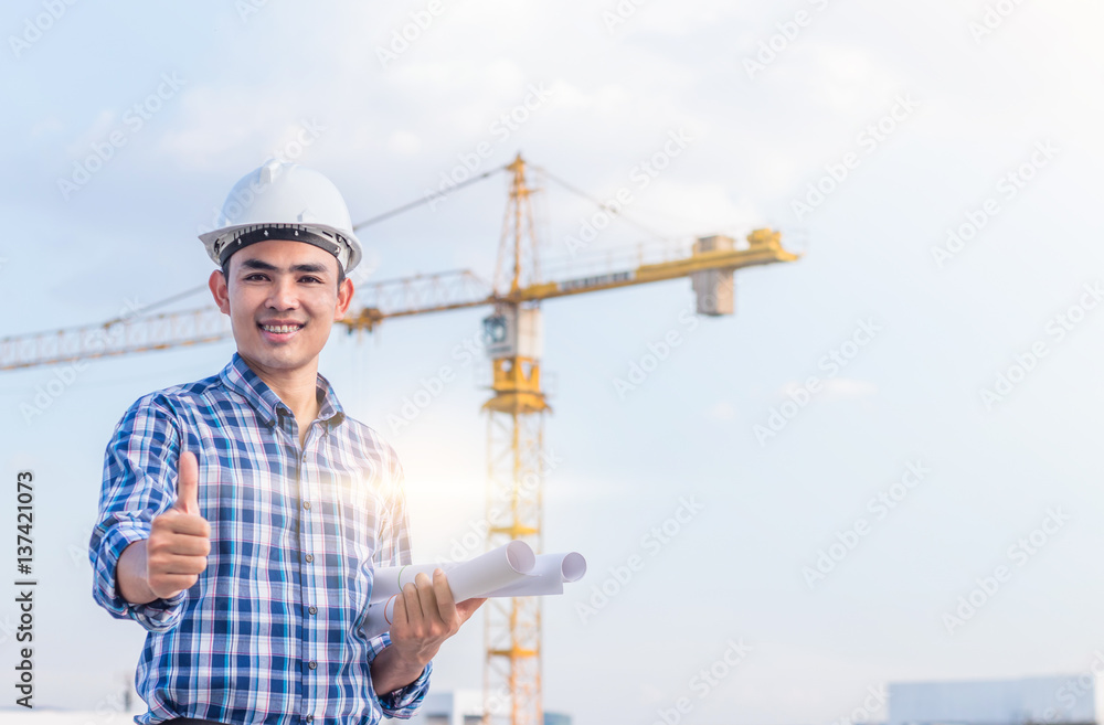 Portrait of engineer wear a white safety helmet and hold the blueprint with construction site and crane background. He has smile because his project were success. Portrait of engineer wear a white safety helmet and hold the blueprint with construction site and crane background. He has smile because his project were success.