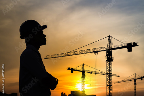 portrait of engineer silhouette wear a helmet at construction site with crane background and sunset