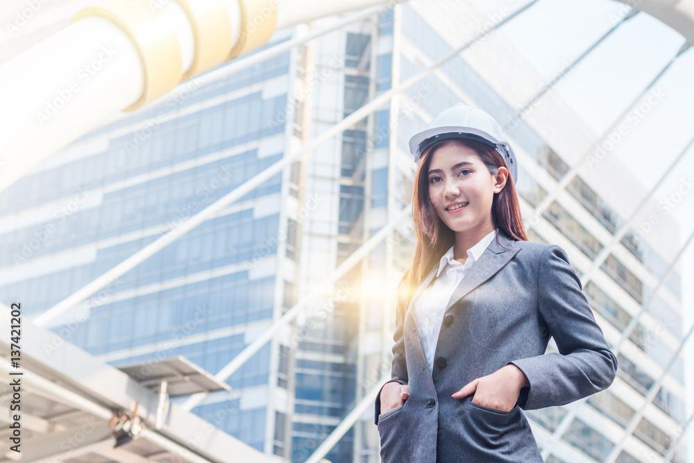 Portrait of beautiful young engineer woman wear a white safety helmet smiling with commitment to success at downtown with building background Portrait of beautiful young engineer woman wear a white safety helmet smiling with commitment to success at downtown with building background