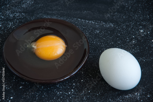 Whole eggs and yolk on a black background sprinkled with flour
