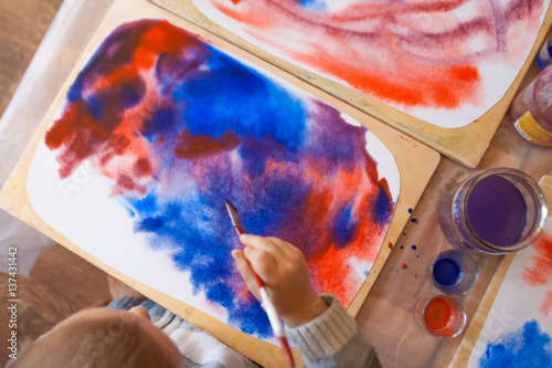 Close-up of watercolor wet-on-wet paints with little boy's head and hand holding paintbrush and drawing in Waldorf kindergarten photo