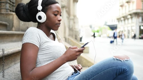 Young beautiful black woman outdoor listening music with head phones and smart phone hand hold, smiling - relaxing, happiness, technology concept
