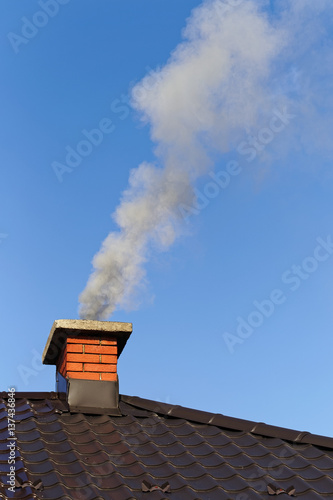 Smoke from brick chimney on the roof against the blue sky