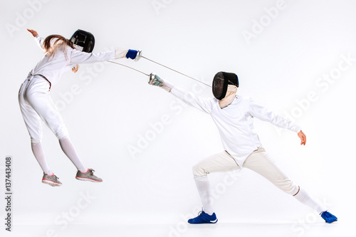 The woman and man wearing fencing suit practicing with sword against gray